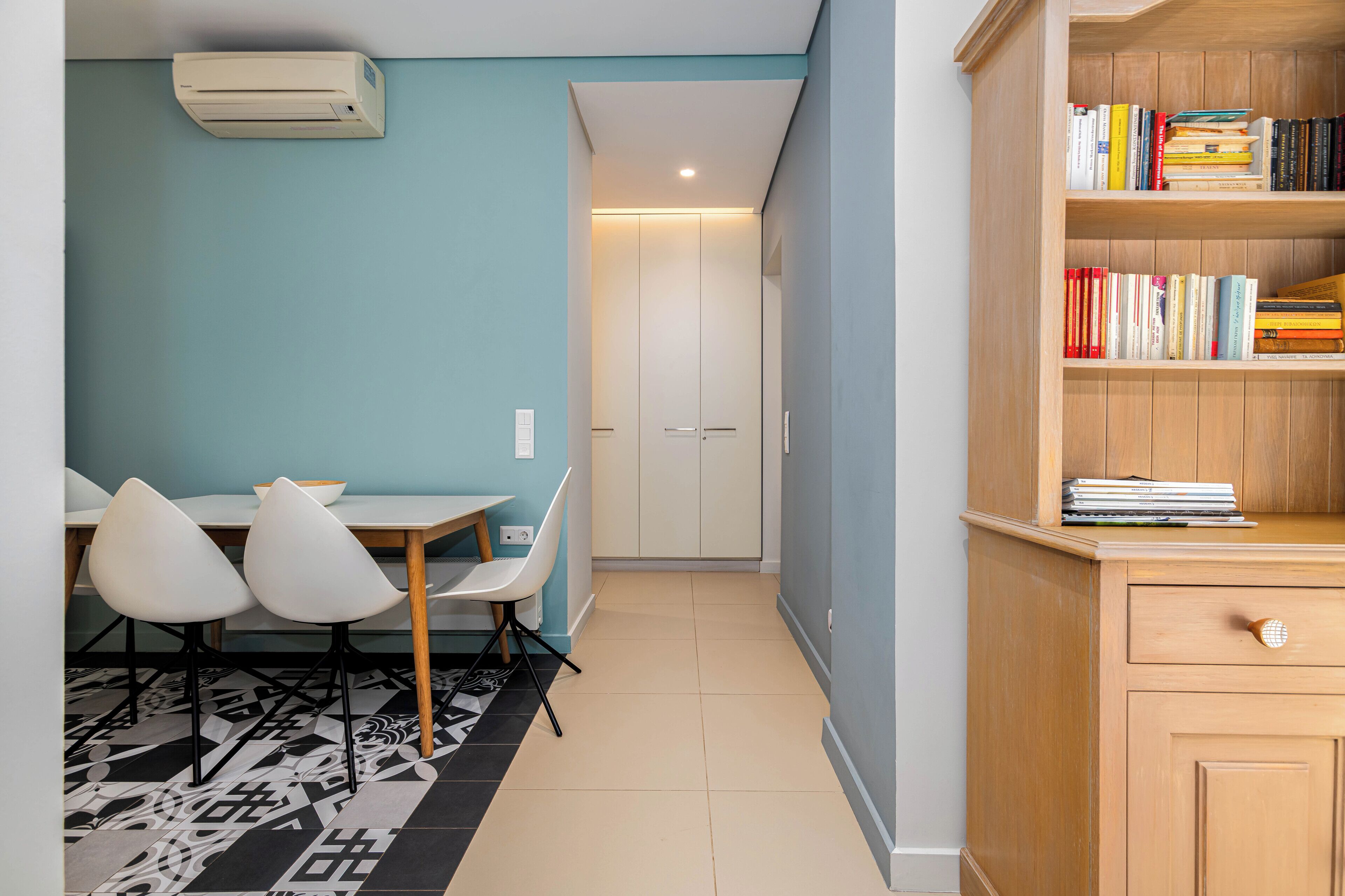 A room with a dining table, two chairs, a bookshelf, and a door leading to another room.