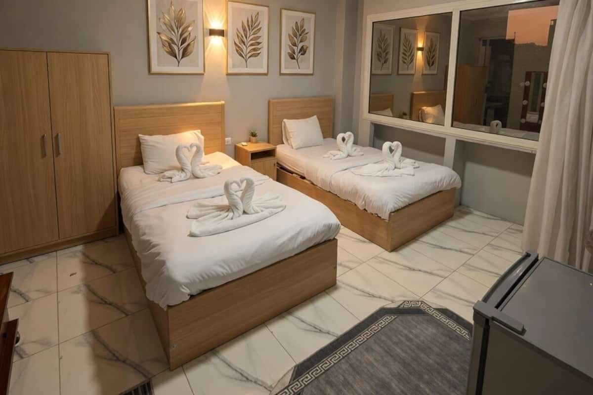 Habitación de hotel con dos camas, un armario, un espejo y obras de arte en las paredes.