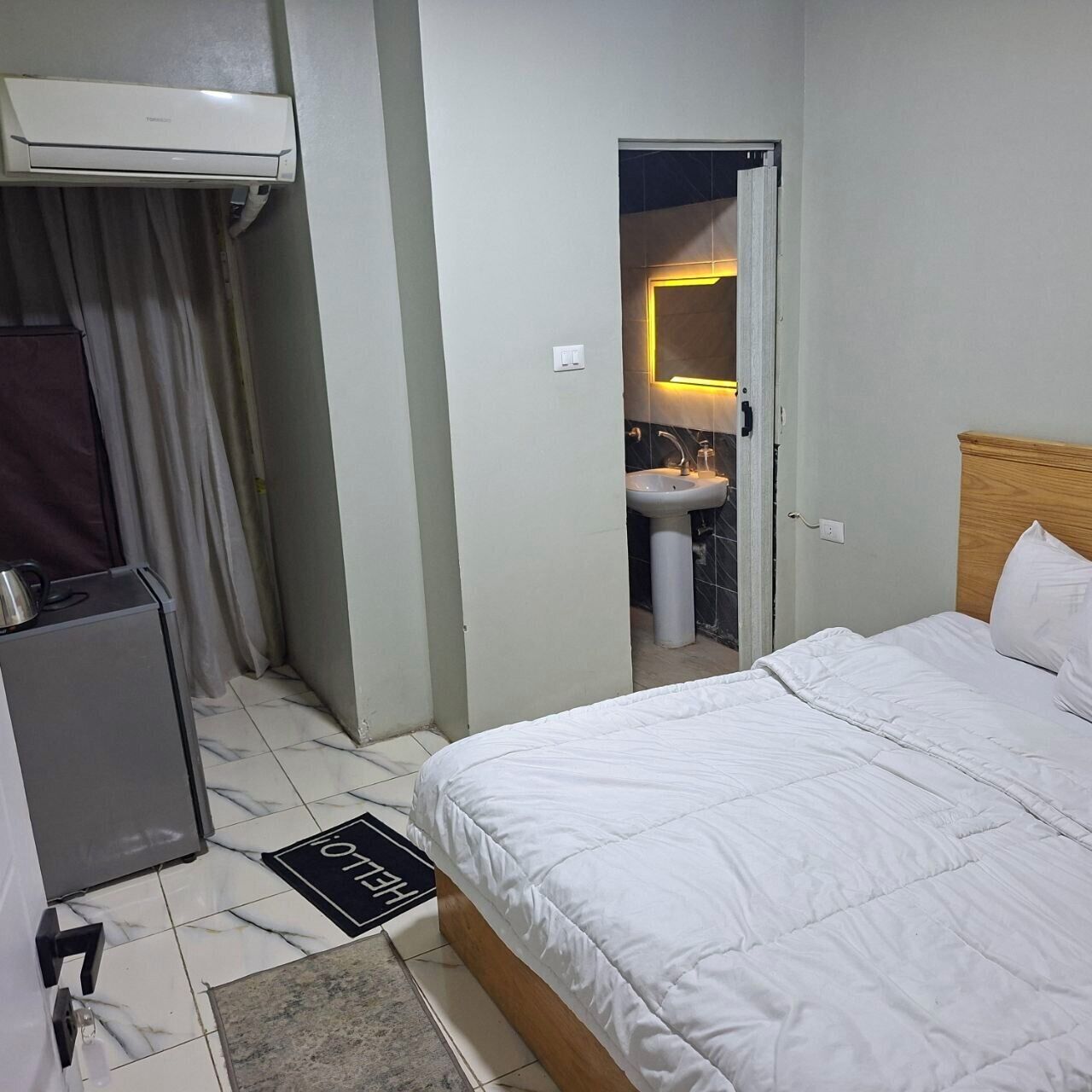 A hotel room with a bed, a sink, and an air conditioning unit.