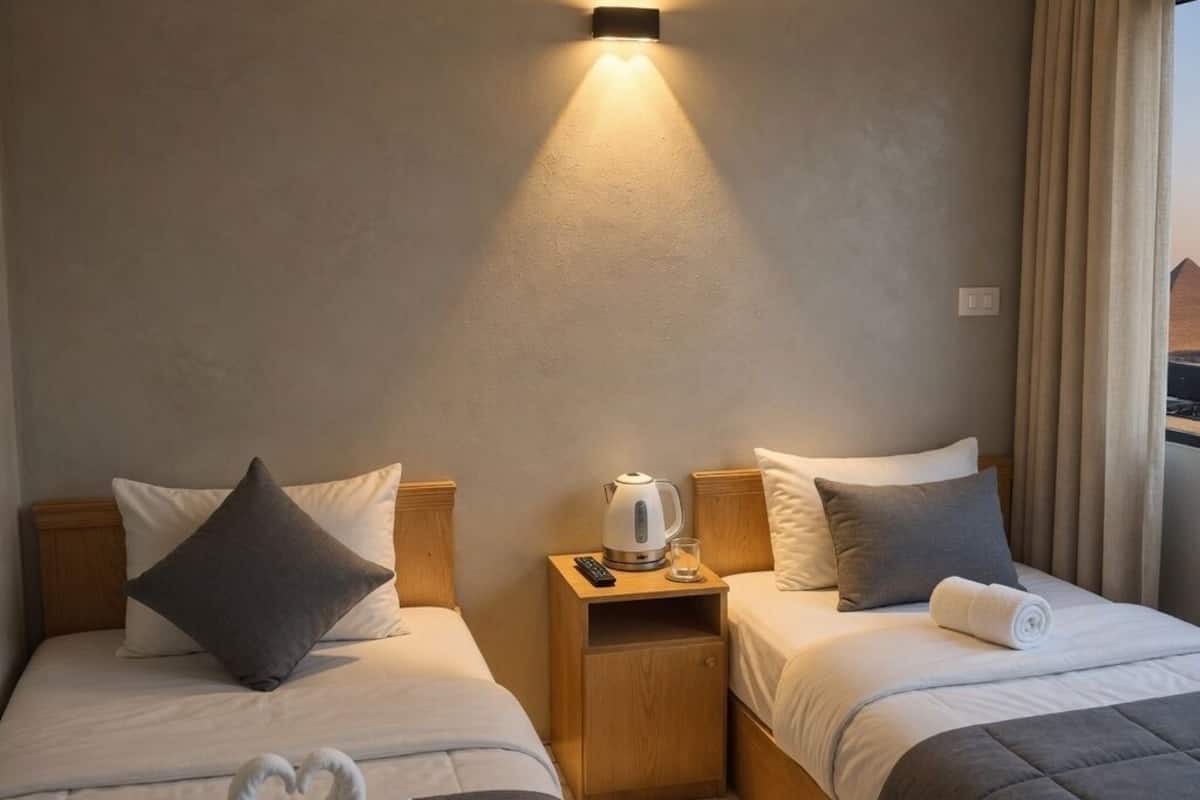 Una habitación de hotel con dos camas, una mesita de noche con hervidor y un aplique de pared.