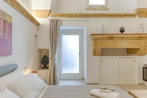 A bedroom with a bed, a nightstand, a window with curtains, a fireplace, and a door leading to another room. - Room 'Casa Sant'Anna 1' with Air Conditioning (Presicce)