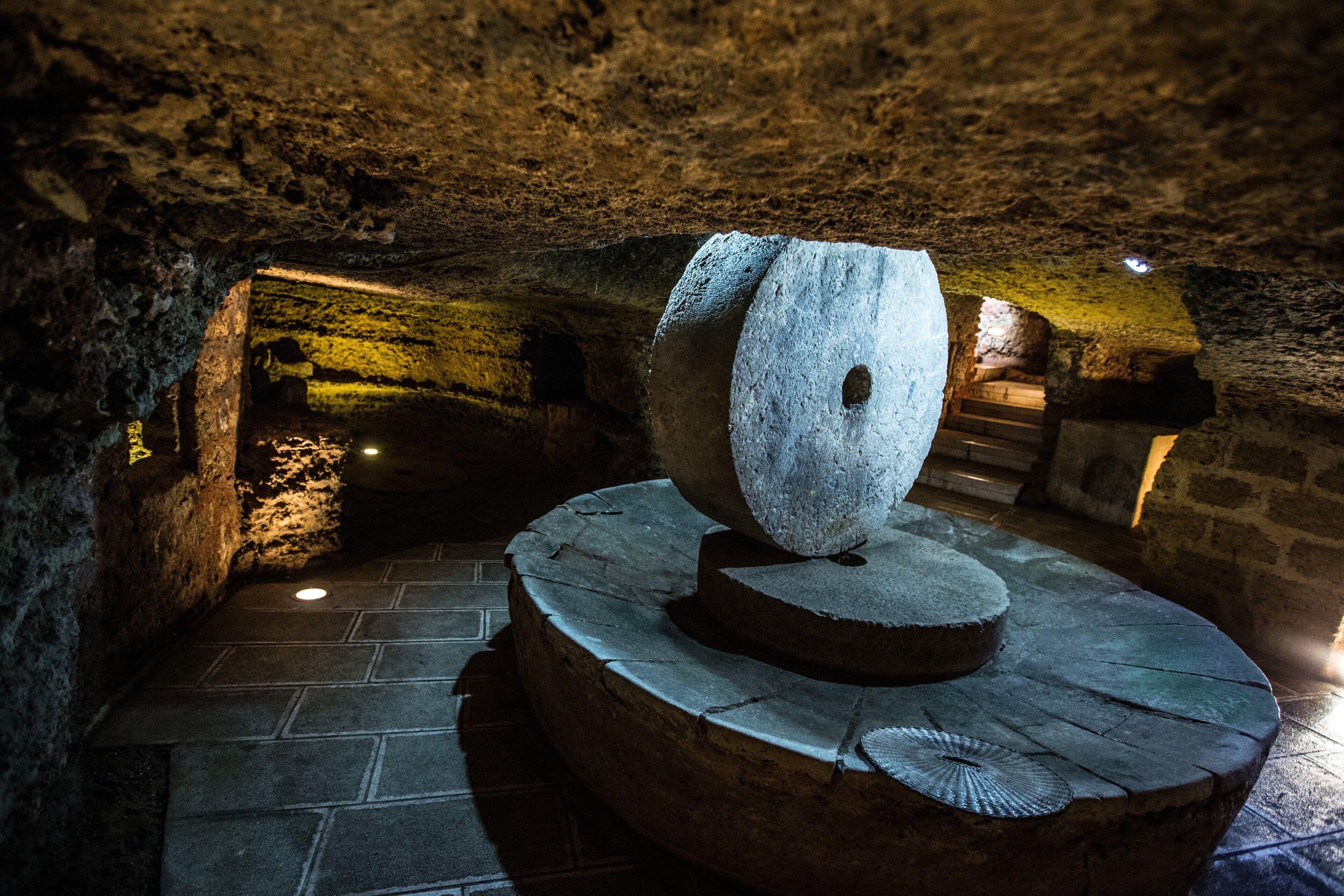 Ein Steinkunstwerk auf einer runden Plattform in einer schattenhaften Höhle mit Steinwänden und Fliesenboden.