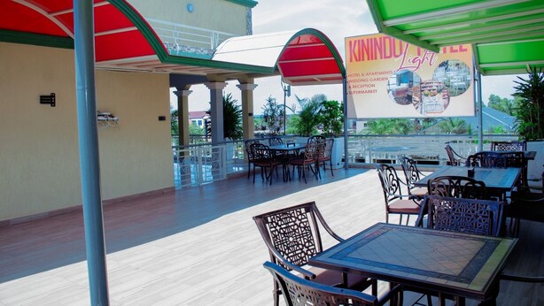 A covered outdoor seating area with tables and chairs, a view of the cityscape, and a sign for Kininduight Hotel & Apartments. - Kinindo Light Hotel (Bujumbura)