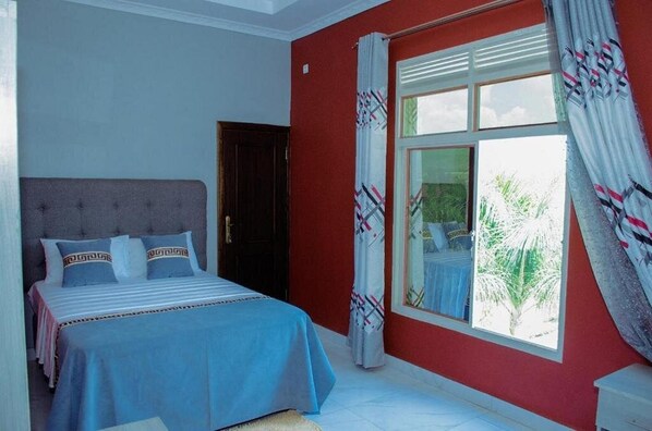 A bedroom with a bed, a window with curtains, and a door.