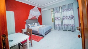 A bedroom with a bed, a table, a chair, a mosquito net, and curtains. - Kinindo Light Hotel (Bujumbura)