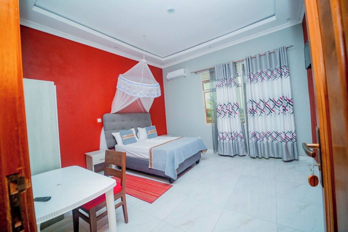 A bedroom with a bed, a table, a chair, a mosquito net, and curtains.