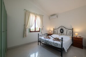 Une chambre à coucher avec un lit, des tables de chevet, une fenêtre avec des rideaux, un climatiseur et une porte verte.