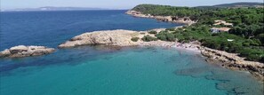 Une zone côtière caractérisée par des eaux turquoise et limpides, un littoral rocheux et une plage parsemée de parasols.