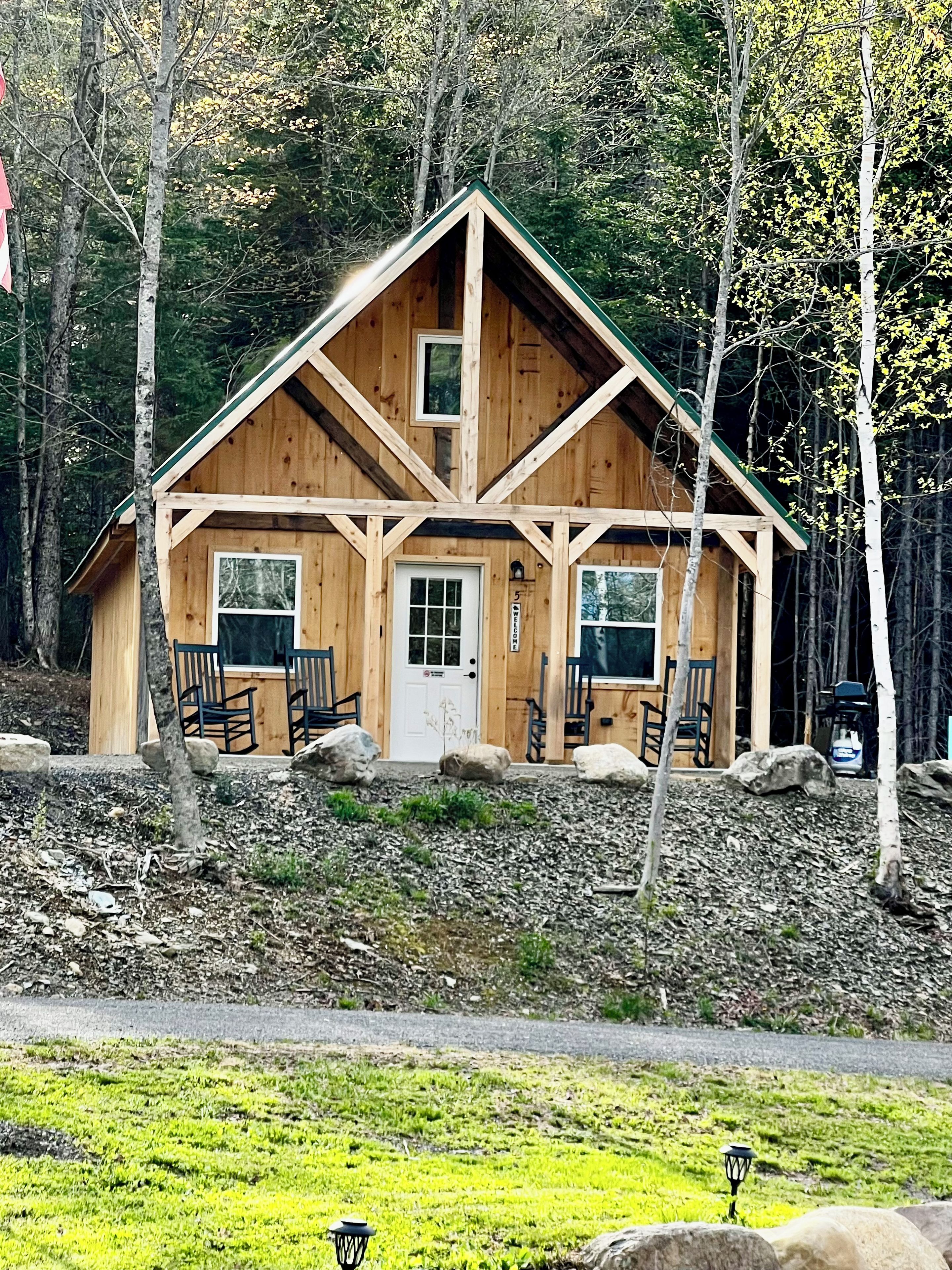 A wooden cabin with a pitched roof, a front door, and two windows.