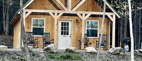 A wooden cabin with a pitched roof, a front door, and two windows.
