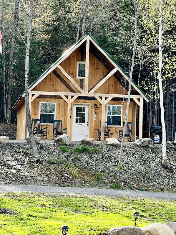 Una cabaña de madera con techo inclinado, una puerta principal y dos ventanas.