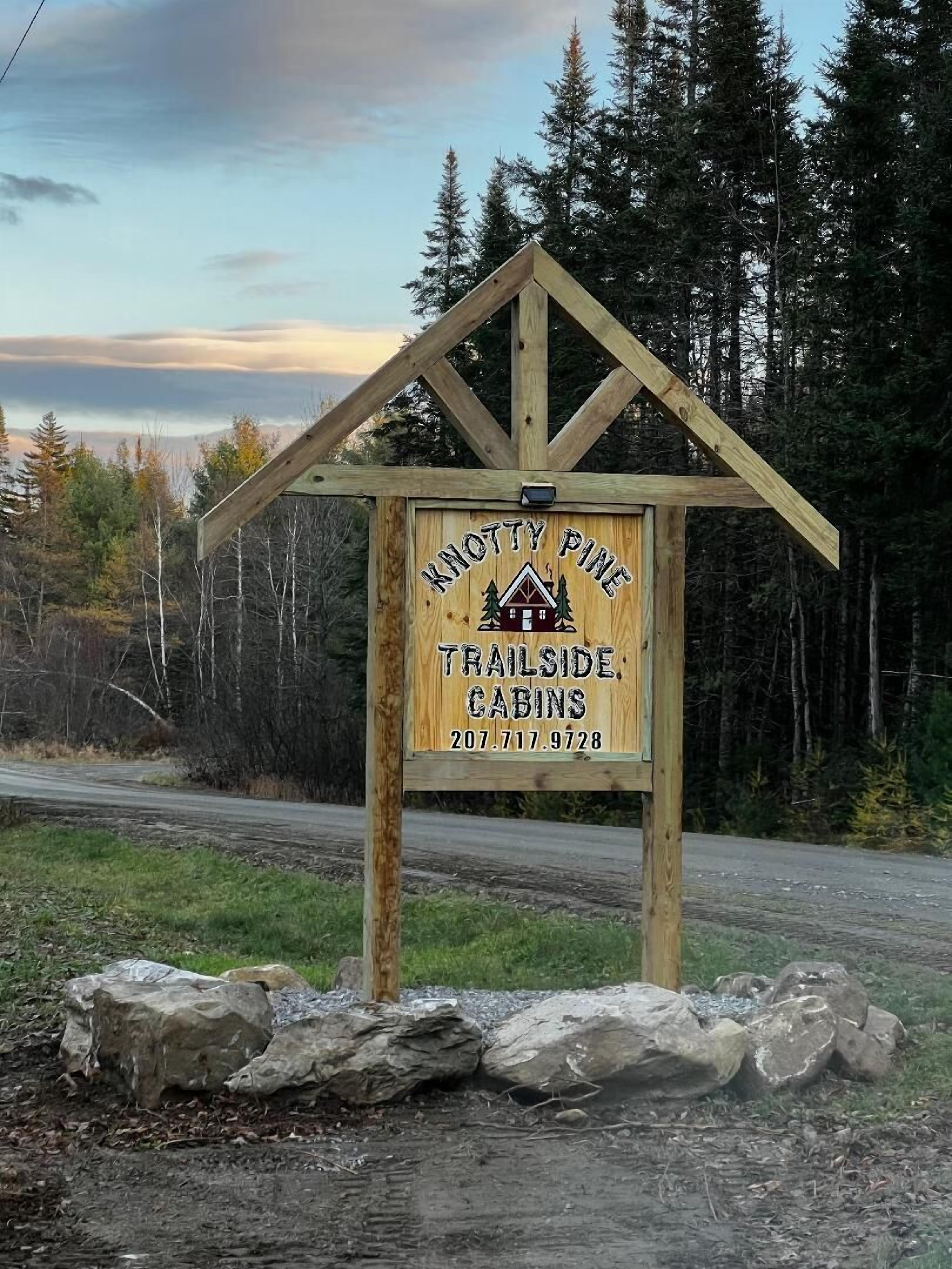 A wooden sign with 'KNOTTY PINE TRAILSIDE CABINS' and a phone number.