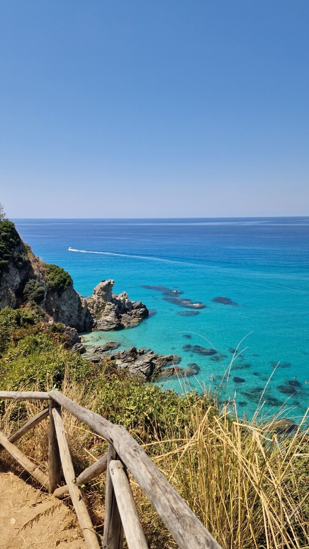 A coastal landscape with clear blue waters, rocky outcrops, and a wooden viewing platform.