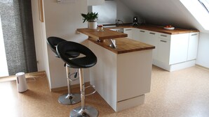 Una cocina compacta con encimera de madera, armarios blancos y una pequeña isla con dos taburetes negros.