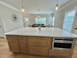 A kitchen with a central island, wooden cabinets, a built-in oven, and pendant lighting. - A newly constructed home with four bedrooms and four bathrooms. (Chamblee)