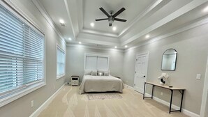 Un dormitorio con cama, escritorio, silla, ventilador de techo y ventana con persianas.