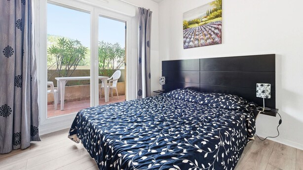 A bedroom with a bed, a headboard, a painting, and a view of an outdoor area. - Charming Studio - Sleeps 2 - bright (Grasse)