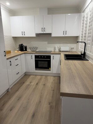 A modern kitchen with white cabinets, a wooden countertop, a built-in oven, a coffee maker, and a kettle. - Beaches, Bays & BBQ Days - Your home base in Burradise (Culburra Beach)
