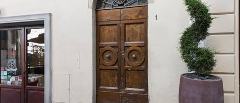 Puerta doble de madera con un arco decorativo encima, una planta en maceta al lado de la puerta y el número '1' en la pared.