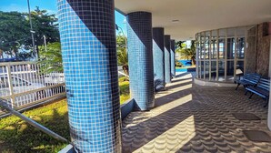 A covered walkway with patterned flooring, blue-tiled columns, and benches. - Studio Pé na Areia - Channel 4 (Santos)