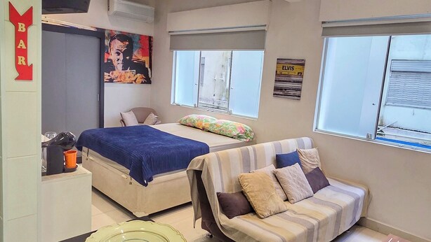 A modern interior with a bed, sofa, dining table, and a kitchen area with a counter. - Studio Pé na Areia - Channel 4 (Santos)