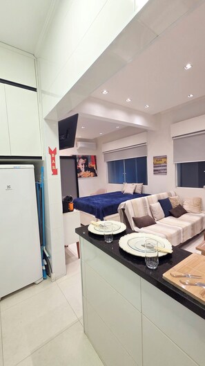 A compact living space with a kitchenette, a dining area, and a bed. - Studio Pé na Areia - Channel 4 (Santos)