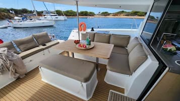 A yacht's deck with a dining area, seating, and a view of the water.