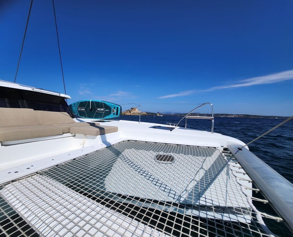 Cubierta de barco con zona de estar acolchada de color blanco, un flotador azul y una barandilla metálica.