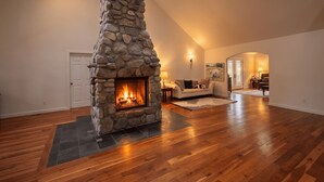 Un salón amplio con chimenea de piedra, suelo de madera y techo alto.