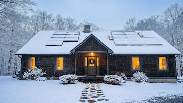 Une cabane en bois avec un toit enneigé, un porche à l’avant et un chemin menant à l’entrée.