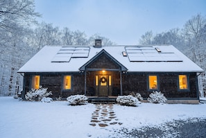Une cabane en bois avec un toit enneigé, un porche à l’avant et un chemin menant à l’entrée.