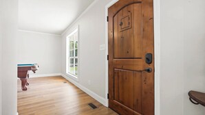 A hallway with wooden flooring, a wooden door, and a window with a view of greenery. - Wildmeade Ranch A Luxury Farmhouse on 18 Acres (Leary)