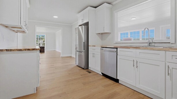 A modern kitchen with white cabinetry, stainless steel appliances, and a wooden countertop. - Wildmeade Ranch A Luxury Farmhouse on 18 Acres (Leary)