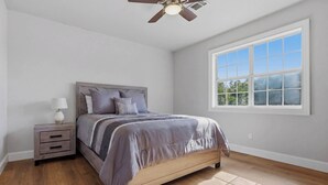 A bedroom with a bed, nightstand, lamp, ceiling fan, and a large window. - Wildmeade Ranch A Luxury Farmhouse on 18 Acres (Leary)