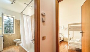 Un bagno con toilette, doccia e finestra vista alberi.
