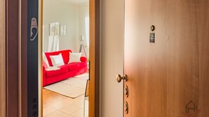 A hotel room with a wooden door, a red sofa, and a white wall with a small sign.