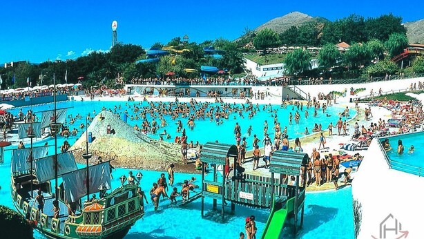 A large outdoor swimming pool with multiple lanes, a lifeguard tower, and a green boat docked nearby.
