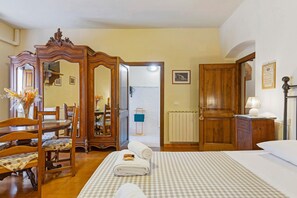 Hotellihuone, jossa on sänky, puinen vaatekaappi, ruokapöytä tuoleineen ja peili.
