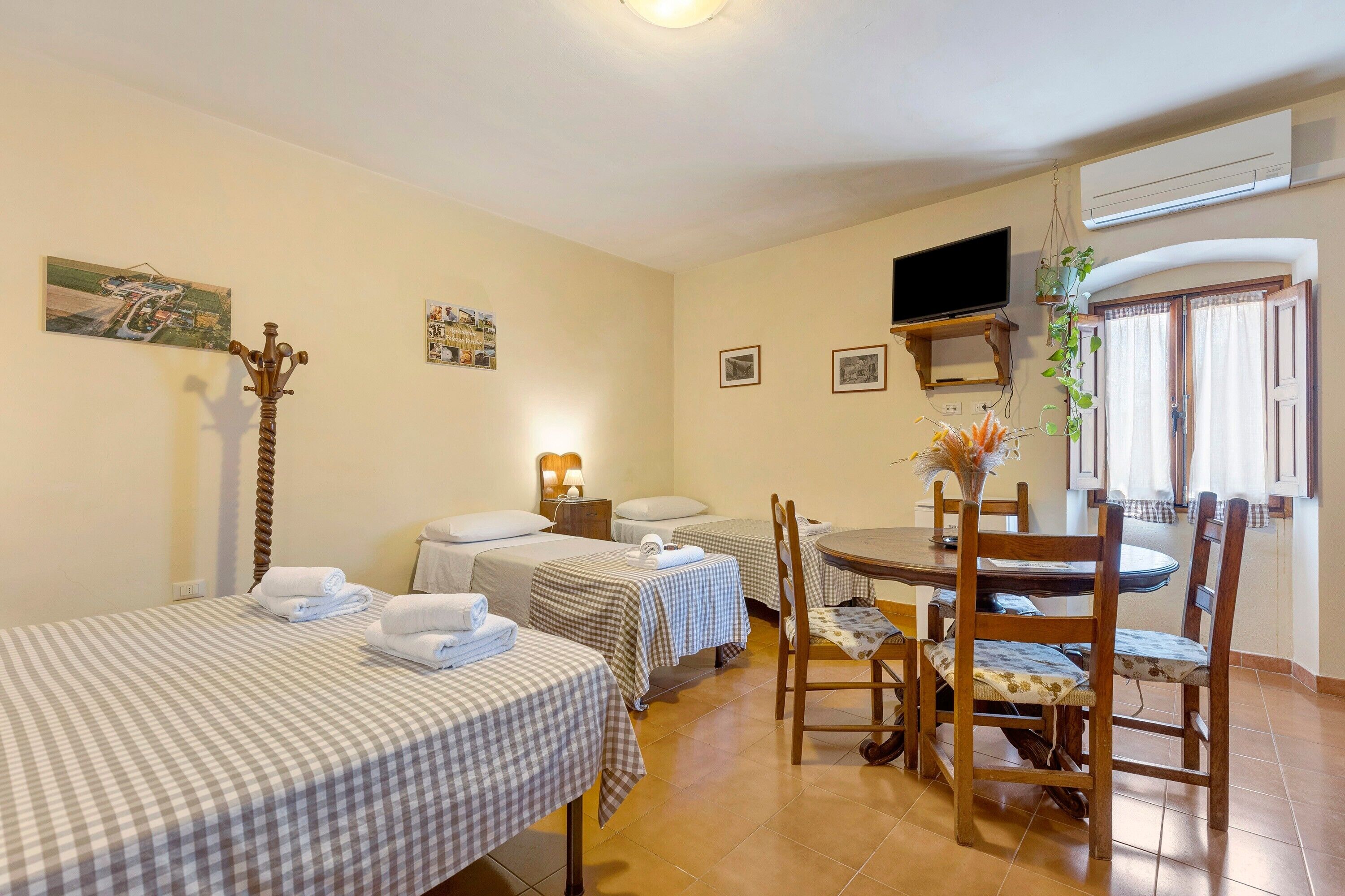 A hotel room with two single beds, a dining table with chairs, a television, and a window with curtains.