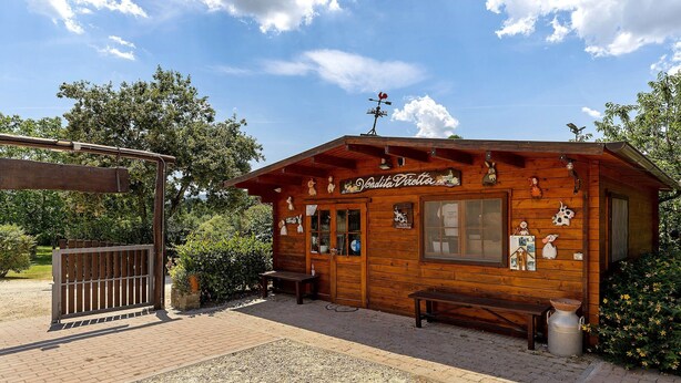 A wooden building with a covered patio, benches, and a metal gate.