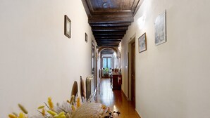 A hallway with a tiled floor, wooden beams on the ceiling, and framed pictures on the walls.