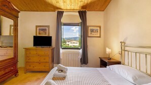 A bedroom with a bed, a dresser, a TV, a window with curtains, and two framed pictures on the wall. - La Spiga Apartment: Spacious Comfort and Accessibility in Mugello (Borgo San Lorenzo)