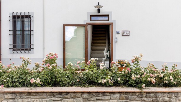 A white building with a stone wall, a wooden door, and a window with a metal grill. - La Spiga Apartment: Spacious Comfort and Accessibility in Mugello (Borgo San Lorenzo)