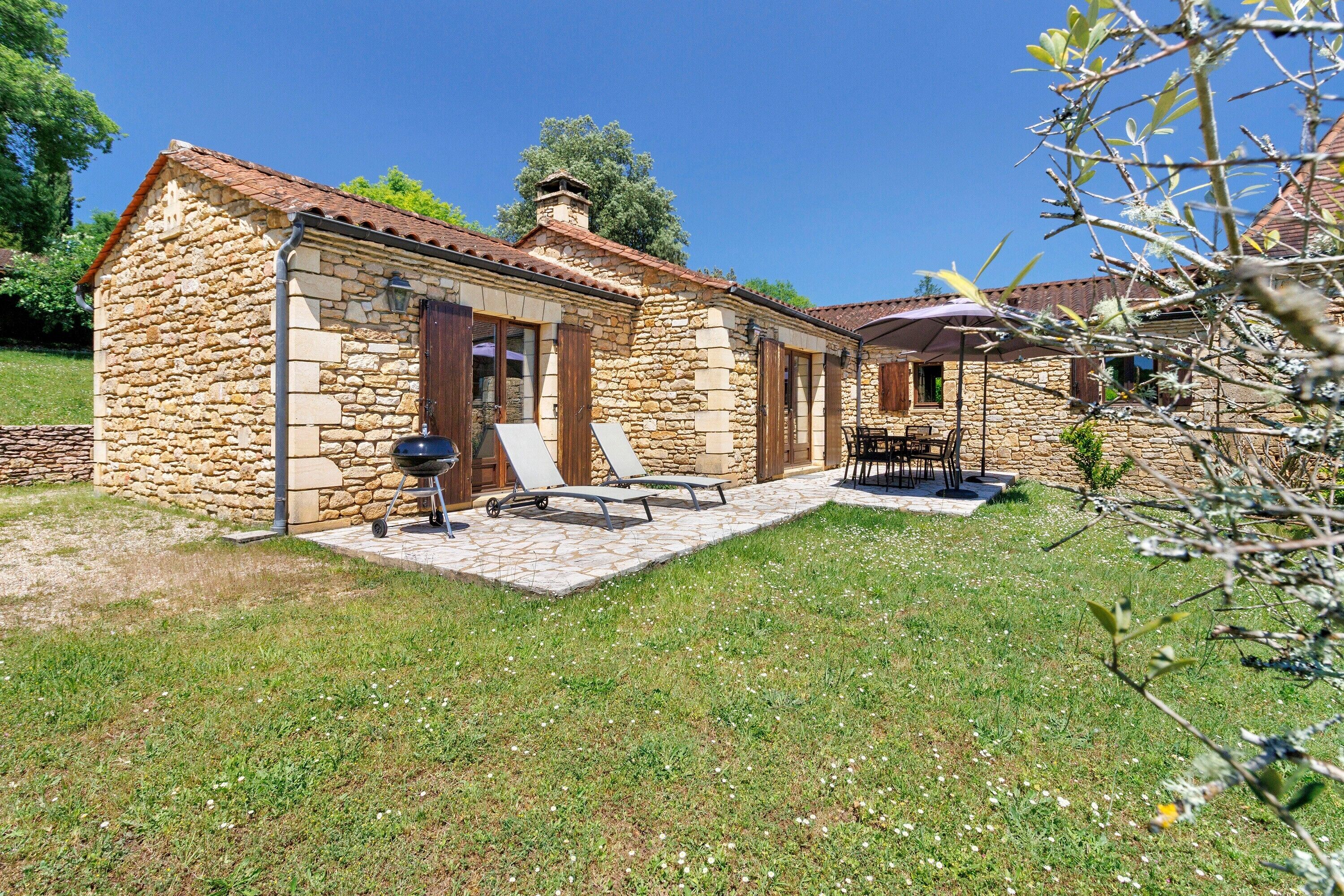 Ein Steinhaus mit Terrasse, Sitzgelegenheiten und Grill.
