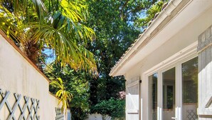 Une terrasse avec un sol en pierre, un mur blanc orné d’un motif en treillis et une porte donnant sur un espace abrité avec des fenêtres.