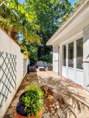 A patio with stone flooring, a white wall with a lattice design, and a door leading to a covered area with windows.