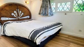 Une chambre à coucher comprenant un lit, un plancher en bois, une tête de lit ornée d’un motif décoratif, une fenêtre avec un rideau et un luminaire fixé au mur.