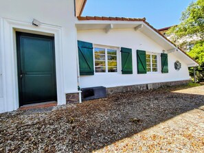 A building with a white facade, green shutters, a stone base, and a gravel driveway.