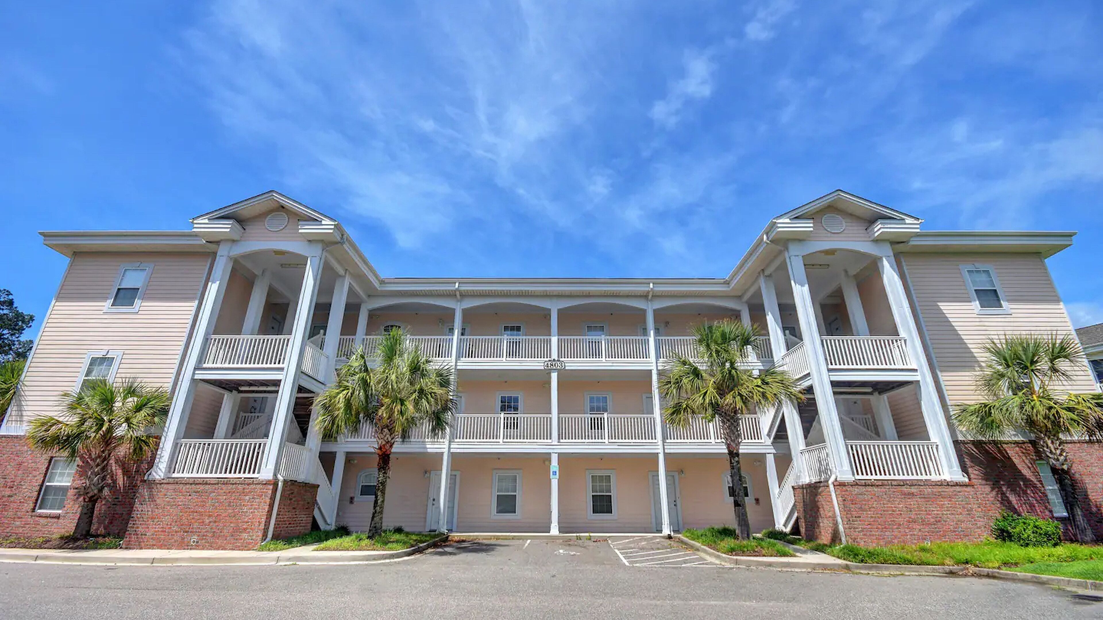 A multi-story building with a central balcony, brick lower floors, and a clear sky.