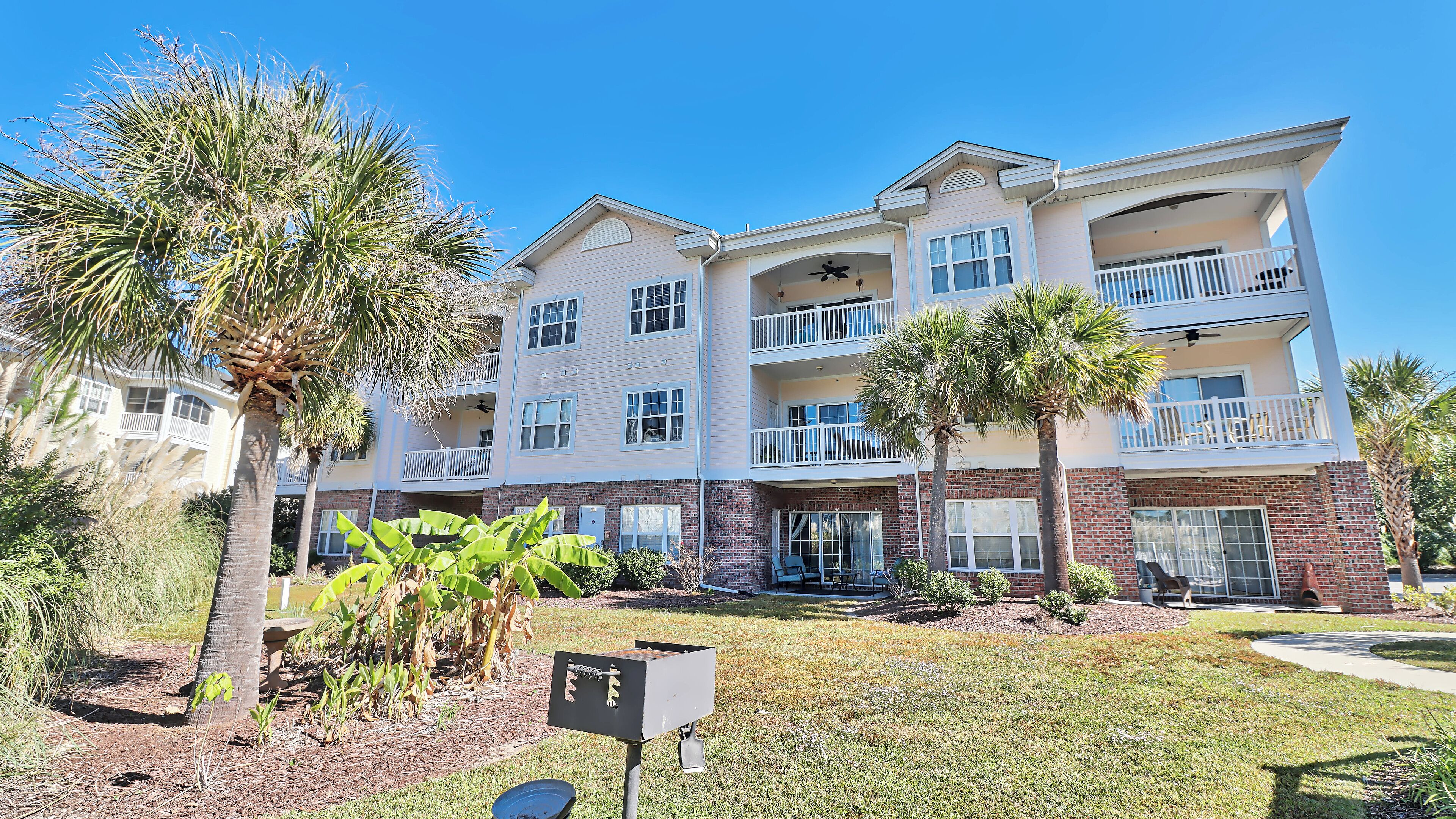 A multi-story building with balconies, a brick facade, and palm trees.